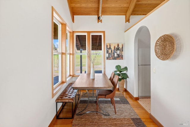 dining room featuring vaulted ceiling with beams, wooden ceiling, and light hardwood / wood-style flooring