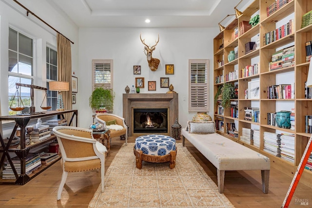 sitting room with a lit fireplace, a tray ceiling, and wood finished floors