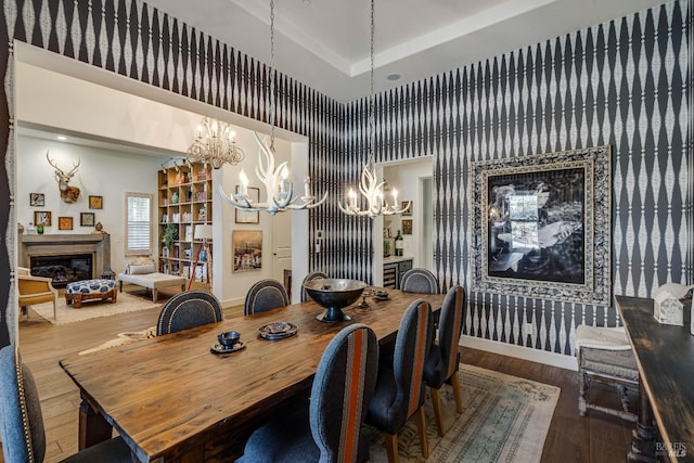 dining room with a notable chandelier, a tray ceiling, wood finished floors, and a glass covered fireplace