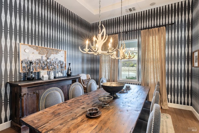 dining area featuring a tray ceiling, visible vents, wood finished floors, a chandelier, and baseboards