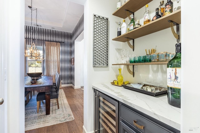 bar featuring wine cooler, dark wood-style flooring, a dry bar, an inviting chandelier, and baseboards