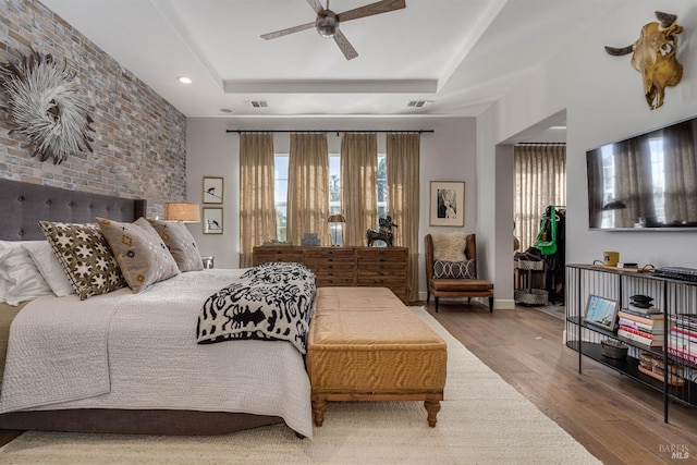 bedroom featuring a tray ceiling, wood finished floors, visible vents, and baseboards