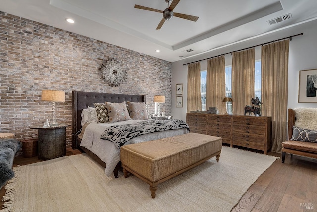 bedroom with recessed lighting, a raised ceiling, visible vents, brick wall, and wood finished floors