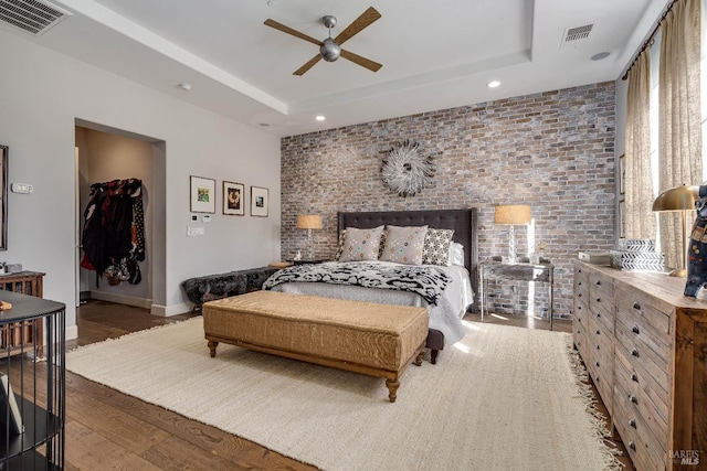 bedroom with brick wall, a tray ceiling, wood finished floors, and visible vents