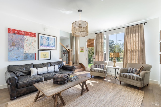 living area with baseboards, stairway, light wood finished floors, and an inviting chandelier