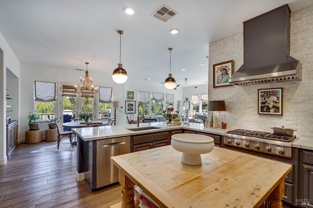 kitchen with stainless steel appliances, a sink, light countertops, wall chimney exhaust hood, and a center island with sink