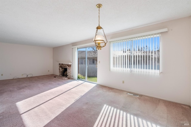 unfurnished living room featuring a brick fireplace, a textured ceiling, a healthy amount of sunlight, and carpet flooring