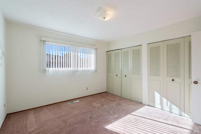 unfurnished bedroom featuring light carpet and two closets