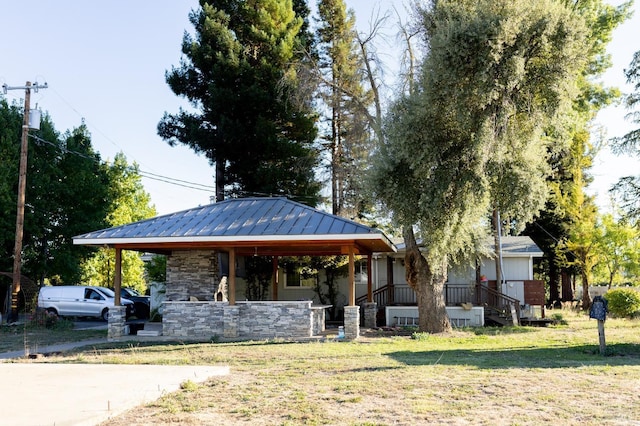 view of front facade with covered porch, a front yard, a standing seam roof, metal roof, and stone siding