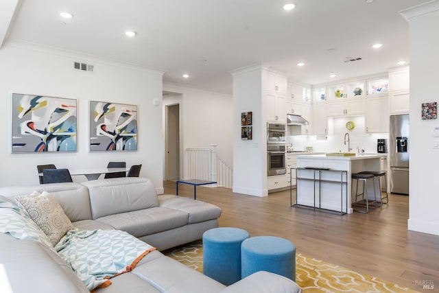 living room with wood-type flooring, sink, and crown molding