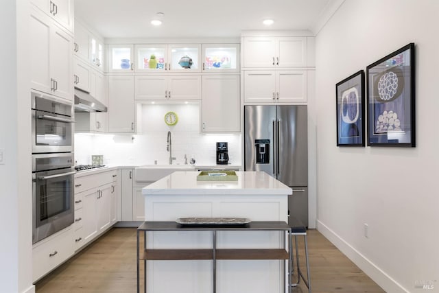 kitchen with a kitchen island, appliances with stainless steel finishes, white cabinetry, sink, and backsplash