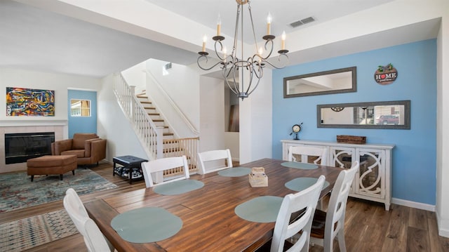 dining area featuring a fireplace, stairs, wood finished floors, and visible vents