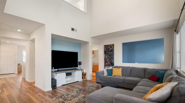 living area featuring a high ceiling, wood finished floors, visible vents, and baseboards