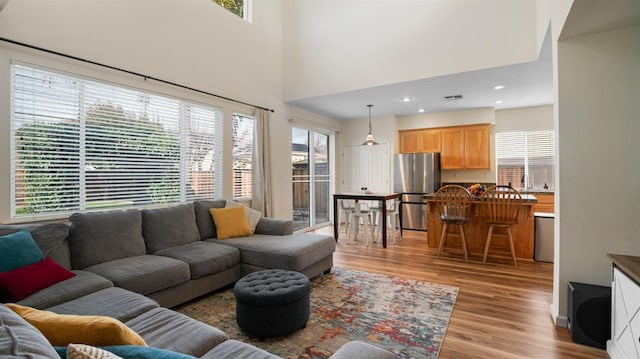 living room with visible vents, recessed lighting, light wood-type flooring, and a towering ceiling