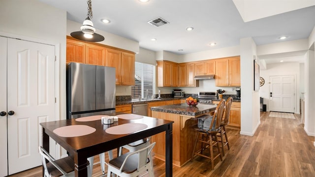 kitchen with a center island, dark countertops, visible vents, under cabinet range hood, and appliances with stainless steel finishes