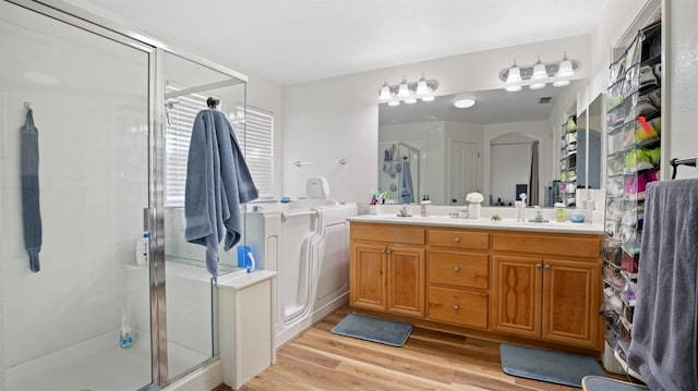 bathroom featuring a stall shower, washer and clothes dryer, a sink, wood finished floors, and double vanity