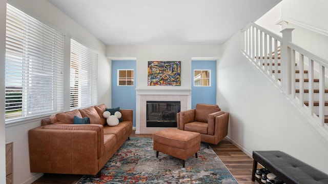 living area featuring a tiled fireplace, stairs, baseboards, and wood finished floors