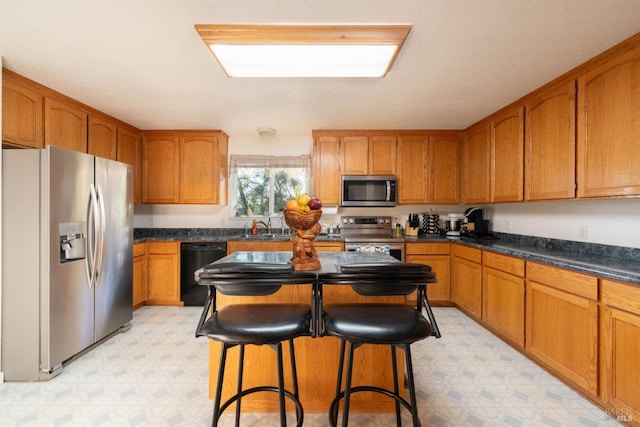 kitchen featuring brown cabinetry, dark countertops, stainless steel appliances, light floors, and a sink