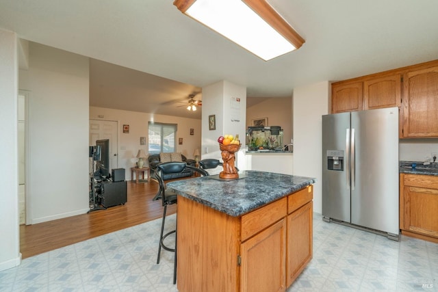 kitchen featuring stainless steel fridge, dark countertops, a breakfast bar area, open floor plan, and light floors