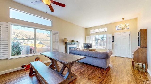 living room with a tiled fireplace, ceiling fan with notable chandelier, wood-type flooring, and a healthy amount of sunlight