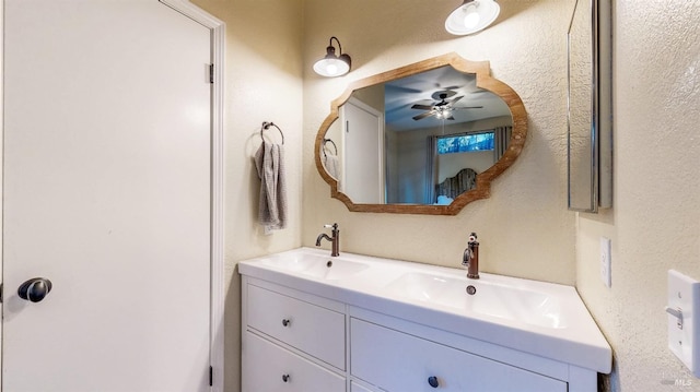 bathroom with a textured wall, double vanity, a sink, and a ceiling fan