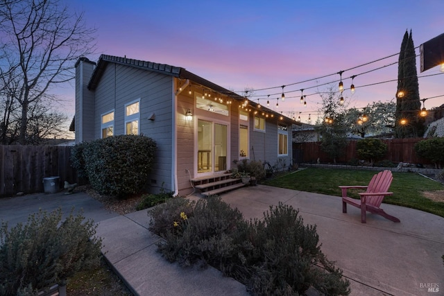 back of property at dusk featuring a patio, a chimney, a fenced backyard, and a lawn