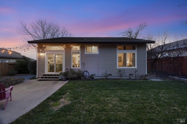 back house at dusk featuring a yard and a patio