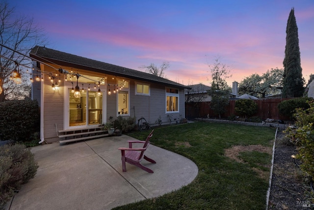 back house at dusk with a lawn and a patio area