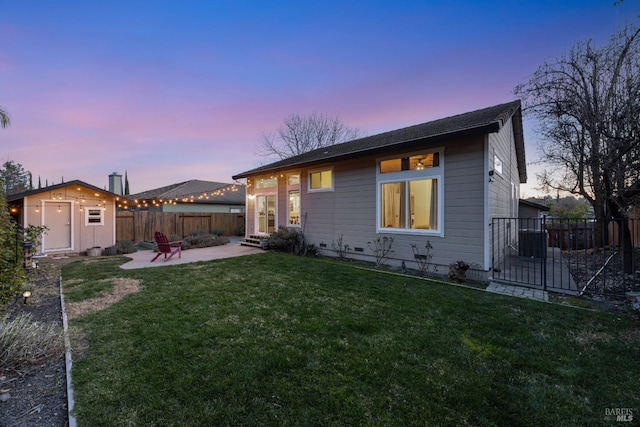 back house at dusk with a shed, a patio area, and a lawn