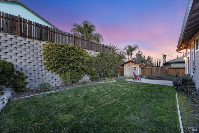 yard at dusk featuring a patio, a storage shed, a fenced backyard, and an outbuilding