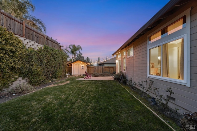 yard at dusk with a storage shed, a fenced backyard, an outdoor structure, and a patio