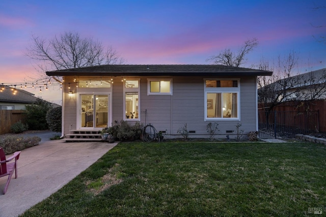 back of house at dusk featuring fence, a lawn, a patio, and crawl space