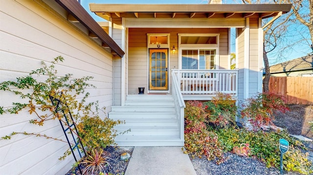 view of exterior entry featuring a porch and fence