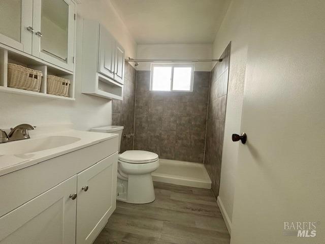 bathroom with vanity, hardwood / wood-style flooring, toilet, and tiled shower