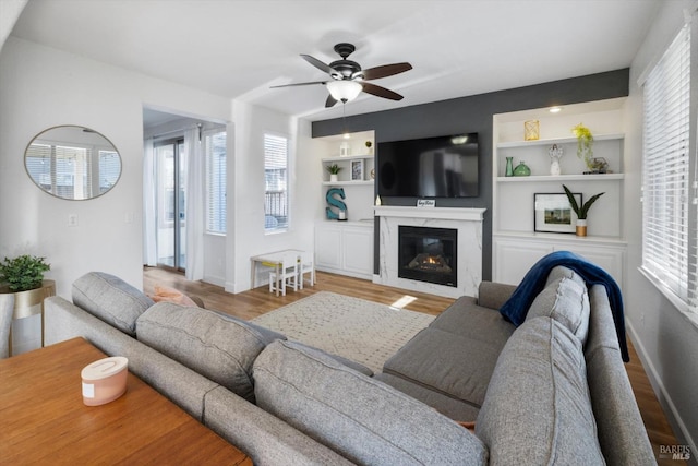 living room with hardwood / wood-style flooring, ceiling fan, a fireplace, and built in shelves