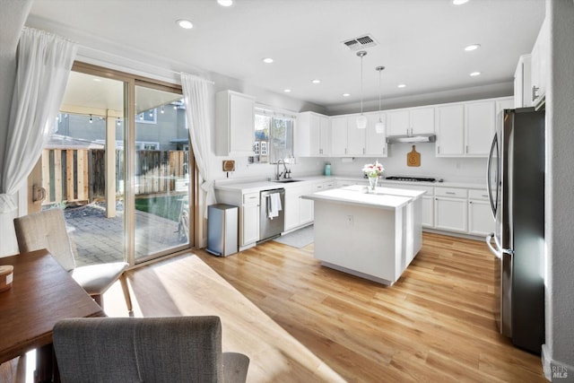 kitchen with pendant lighting, appliances with stainless steel finishes, white cabinetry, a center island, and light wood-type flooring