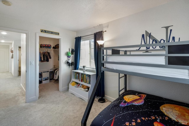 bedroom featuring a walk in closet, light carpet, a textured ceiling, and a closet