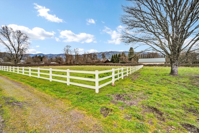 view of yard with a rural view, fence, and a mountain view