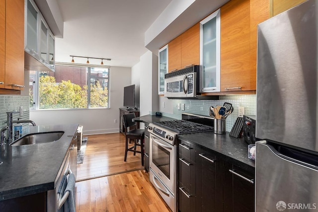 kitchen featuring sink, appliances with stainless steel finishes, dark stone counters, light hardwood / wood-style floors, and backsplash