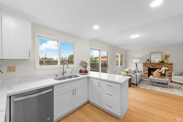 kitchen with sink, dishwasher, white cabinetry, a fireplace, and light wood-type flooring