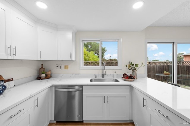 kitchen featuring white cabinetry, sink, stainless steel dishwasher, and light stone counters