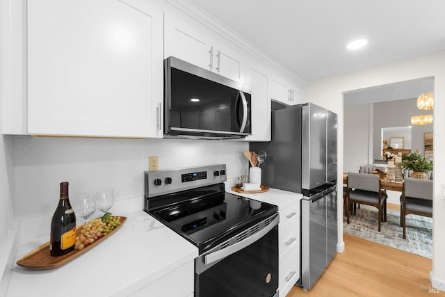 kitchen with appliances with stainless steel finishes, white cabinetry, a chandelier, light stone countertops, and light wood-type flooring