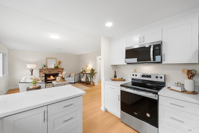 kitchen with appliances with stainless steel finishes, white cabinetry, light hardwood / wood-style floors, light stone countertops, and a brick fireplace