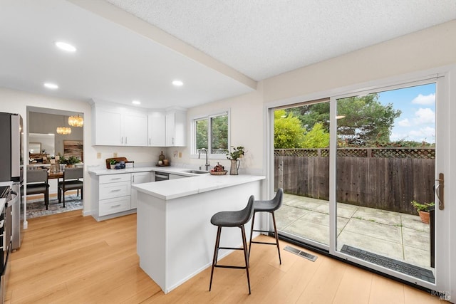 kitchen featuring white cabinetry, sink, a breakfast bar area, kitchen peninsula, and light hardwood / wood-style flooring