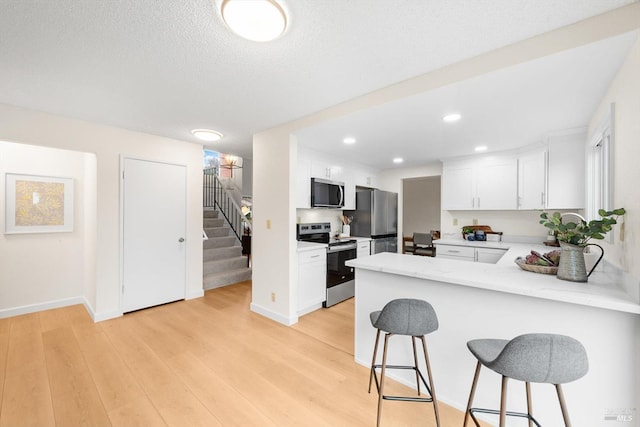 kitchen with a breakfast bar area, white cabinetry, stainless steel appliances, kitchen peninsula, and light wood-type flooring