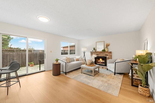 living room with a brick fireplace, a textured ceiling, and light wood-type flooring