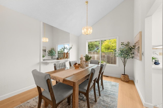 dining space with an inviting chandelier, high vaulted ceiling, and light hardwood / wood-style floors