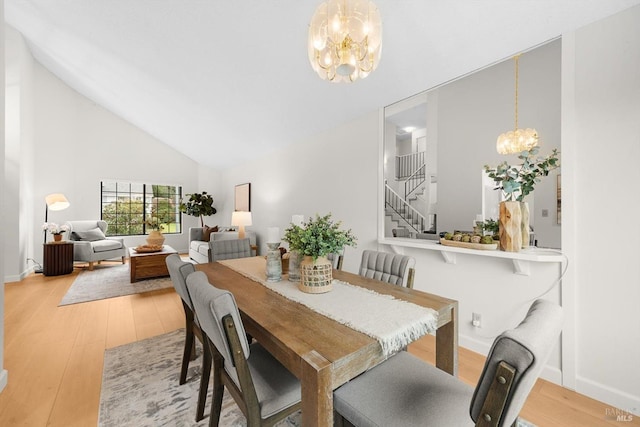 dining space with high vaulted ceiling, an inviting chandelier, and light hardwood / wood-style floors