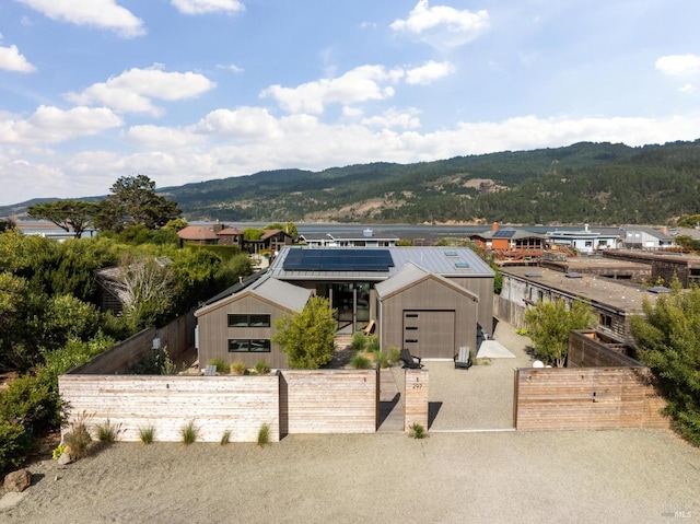 view of front facade featuring a fenced front yard, roof mounted solar panels, a mountain view, and a residential view