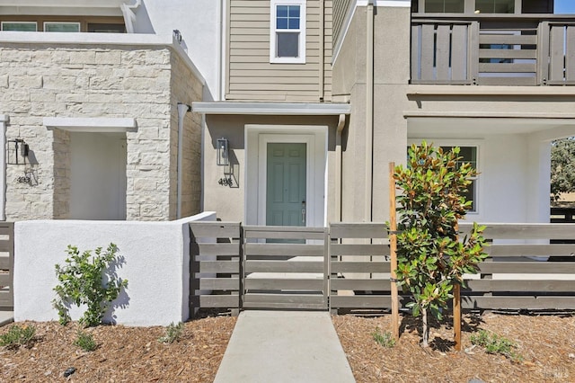 view of exterior entry featuring fence, a balcony, and stucco siding